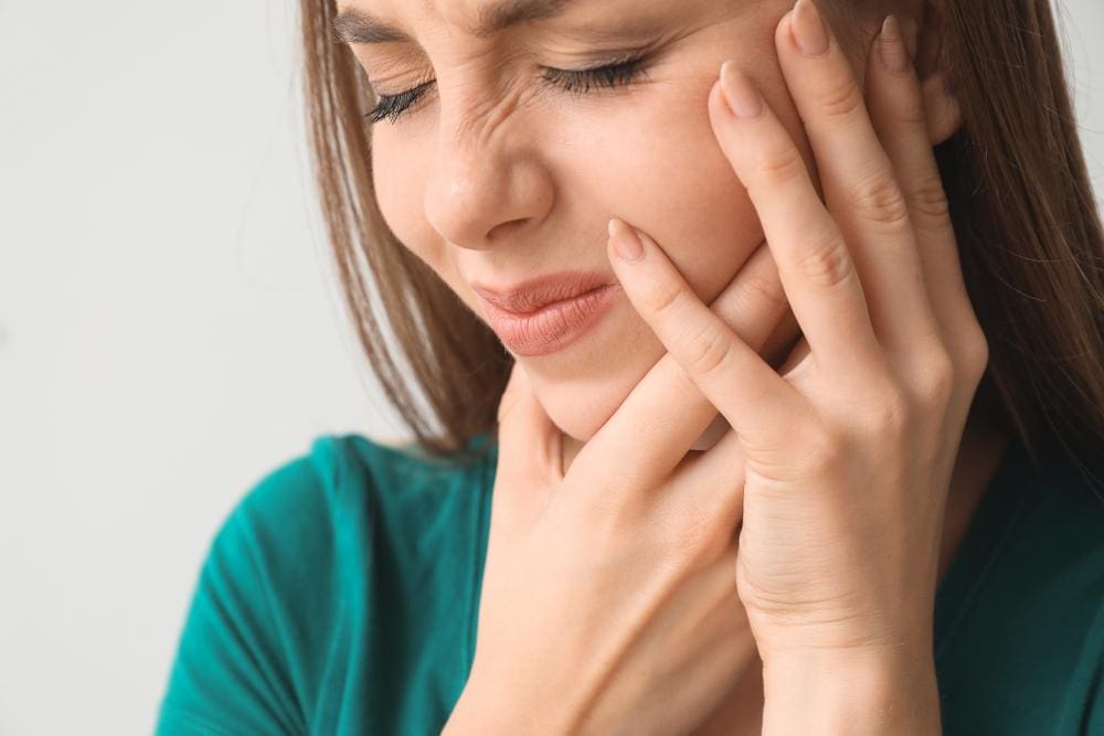 A woman is wincing in pain and clutching her face due to trigeminal neuralgia pain.
