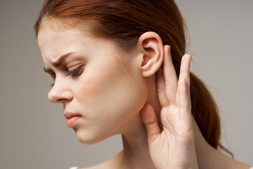 A woman suffering from trigeminal neuralgia pain is holding her hand behind ear, because it hurts. 

