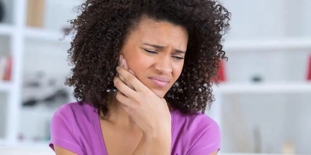 A woman is clutching her face because of trigeminal neuralgia nerve pain.