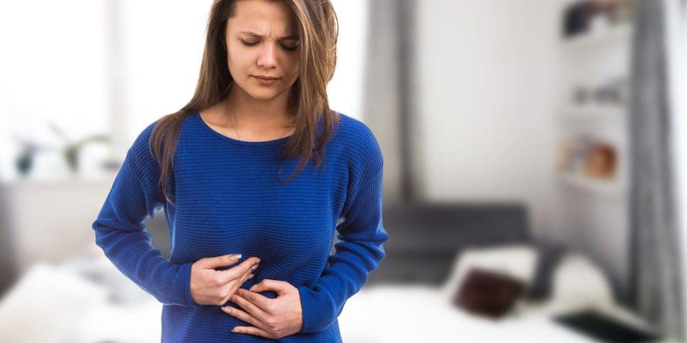 A young woman is holding her stomach because of pain and discomfort caused by bloating.