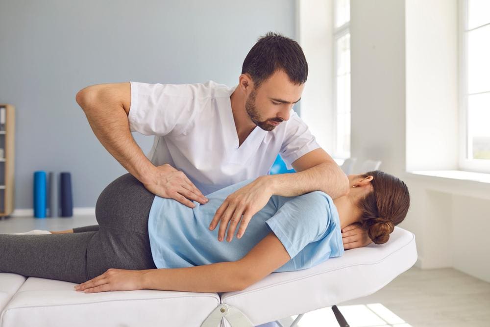 A chiropractor is administering a spinal adjustment on a female patient.