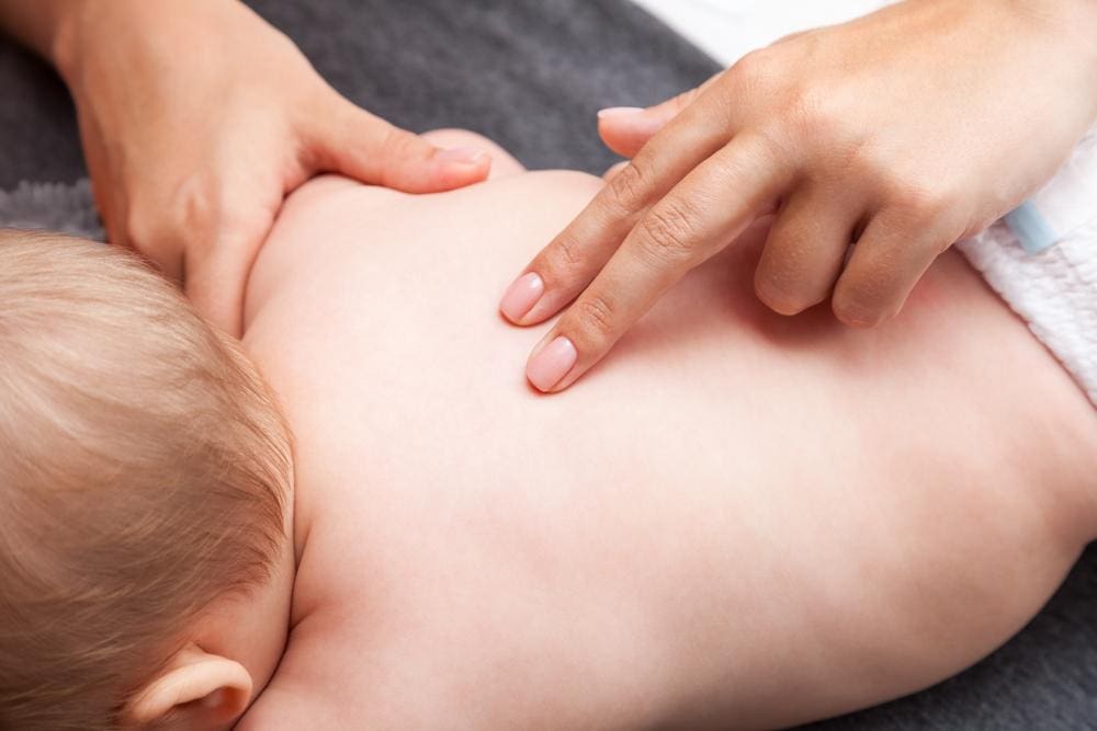 A chiropractor is gently assessing a baby's spinal alignment.