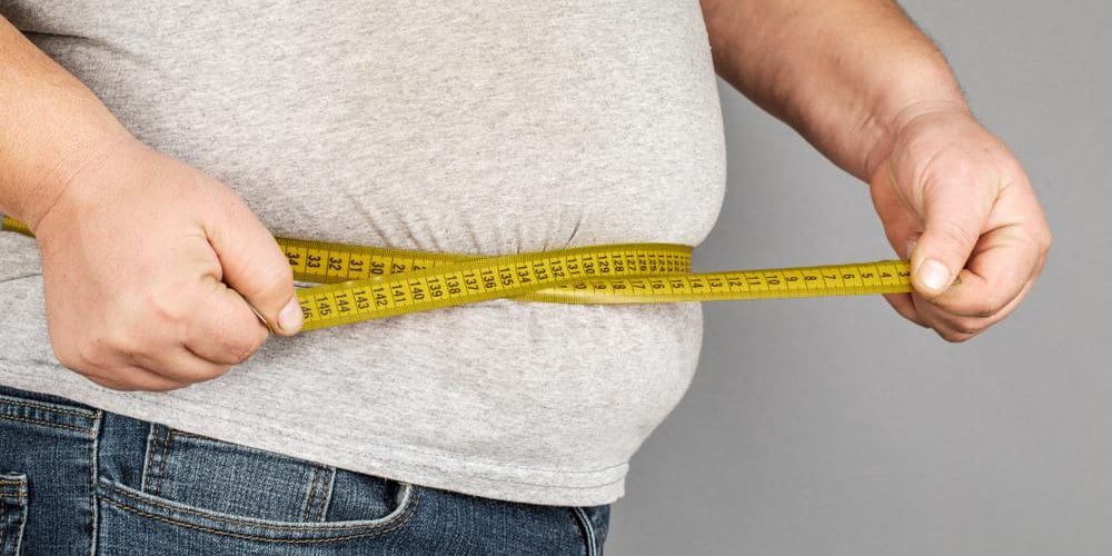 A man struggling with his weight is measuring his waistline with a measuring tape.