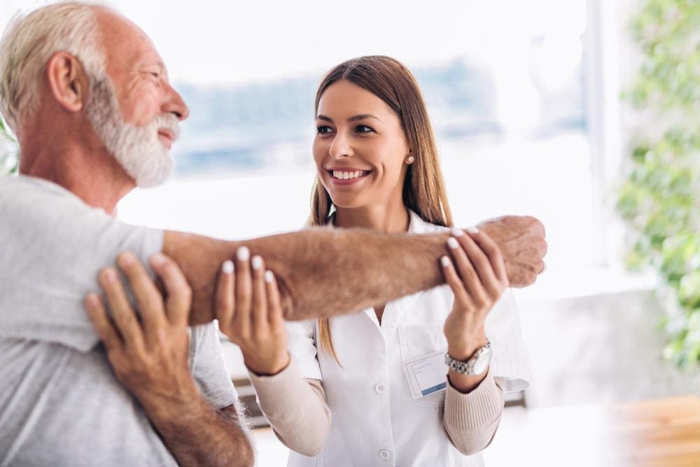 A chiropractor is giving an arm adjustment to an elderly man with tendonitis.