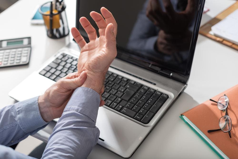 A man has stopped typing and is massaging his wrist because of carpal tunnel pain.