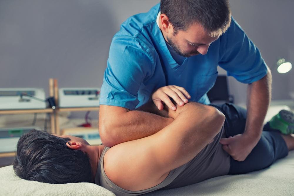 A chiropractor is performing a chiropractic adjustment on a male patient. 