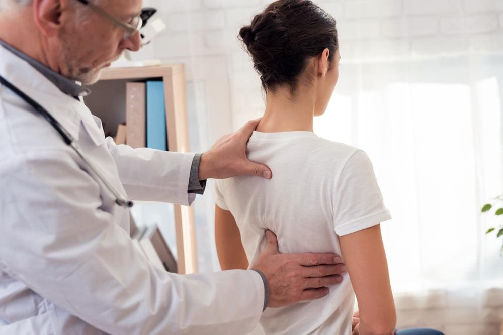A chiropractor is examining a woman's spine after she had back surgery. 