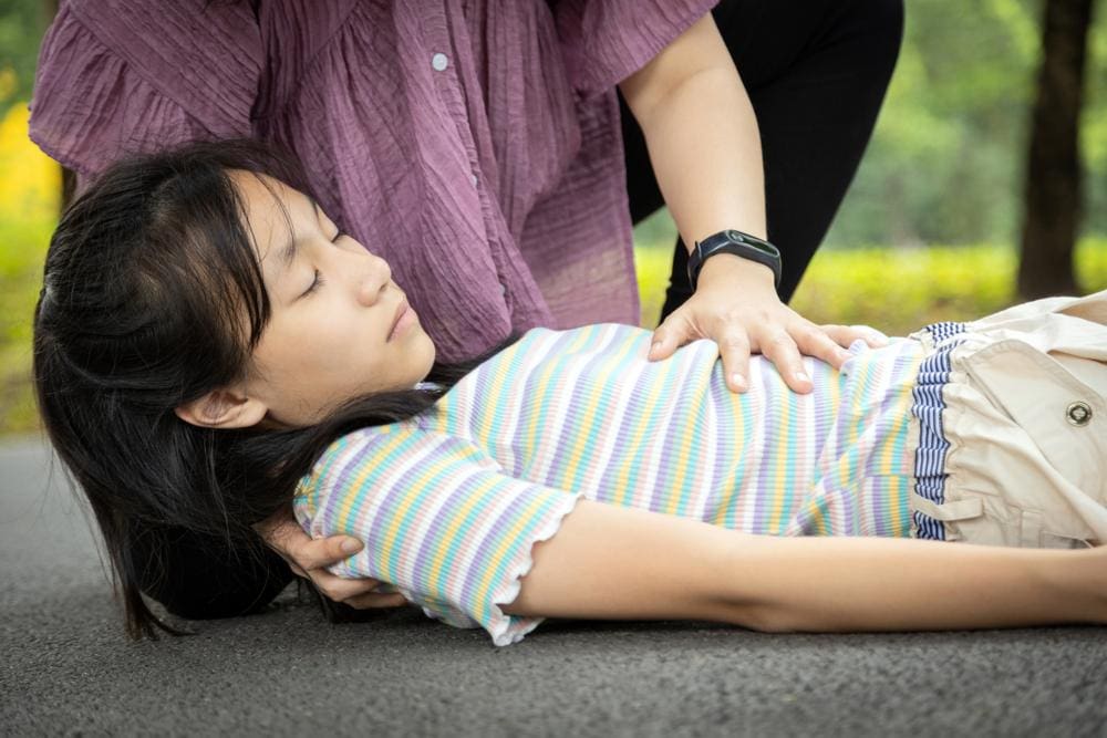 Young girl lying on ground while having an epileptic seizure with mother beside her.

