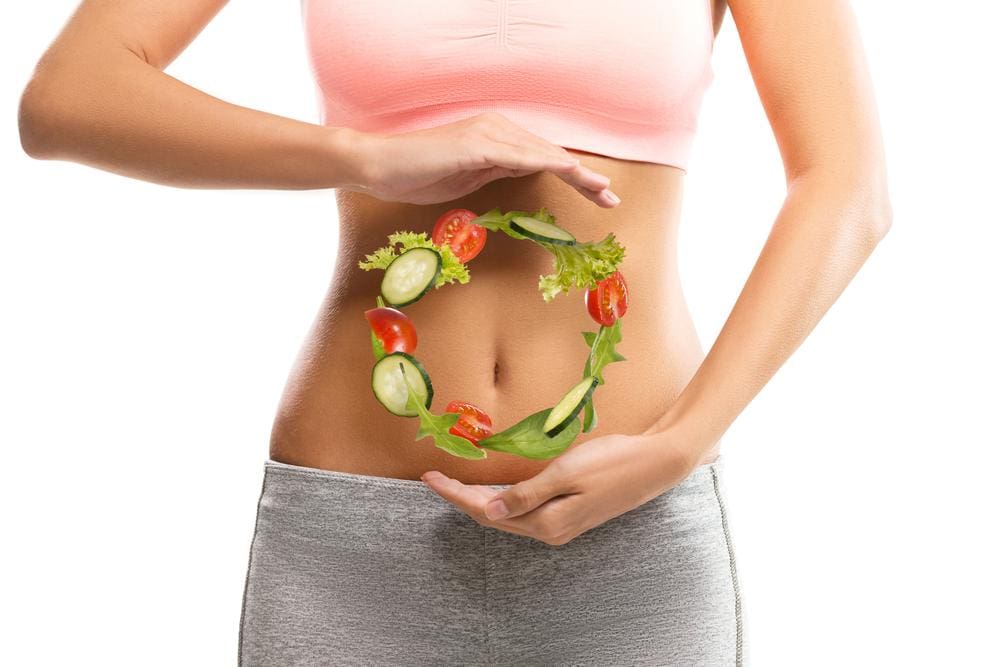 Young woman in athletic clothing holding hands at top and bottom of abdomen with an illustrated circle in vegetables between.
