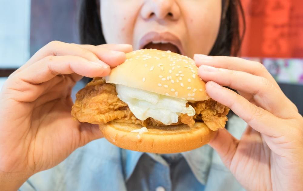 Woman eating a breaded fried chicken sandwich in fast food restaurant.