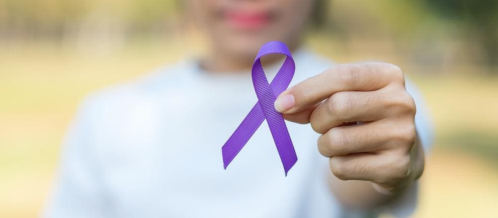Person holding up a purple support ribbon.
