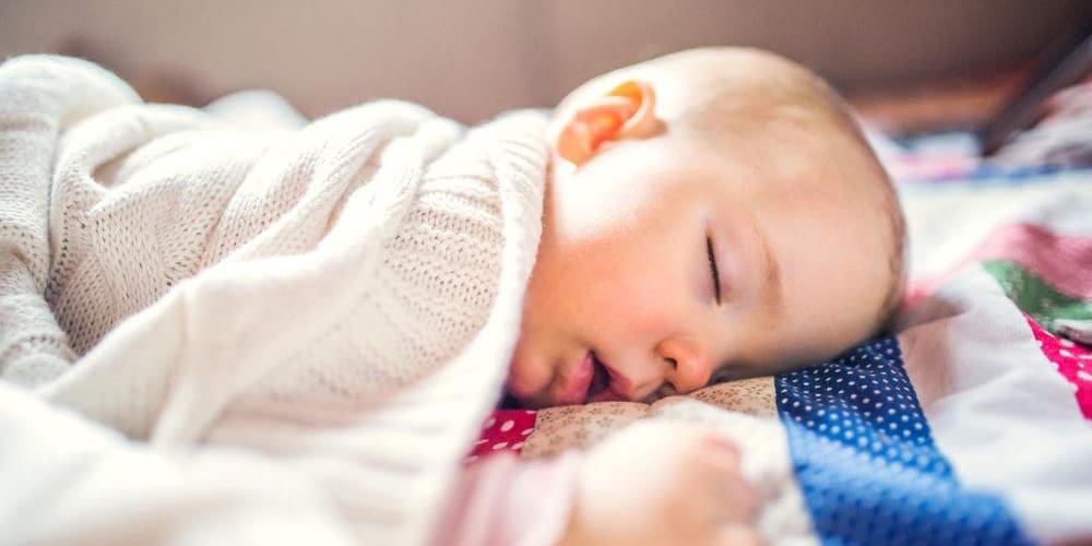 A baby is sleeping on their side in a crib.