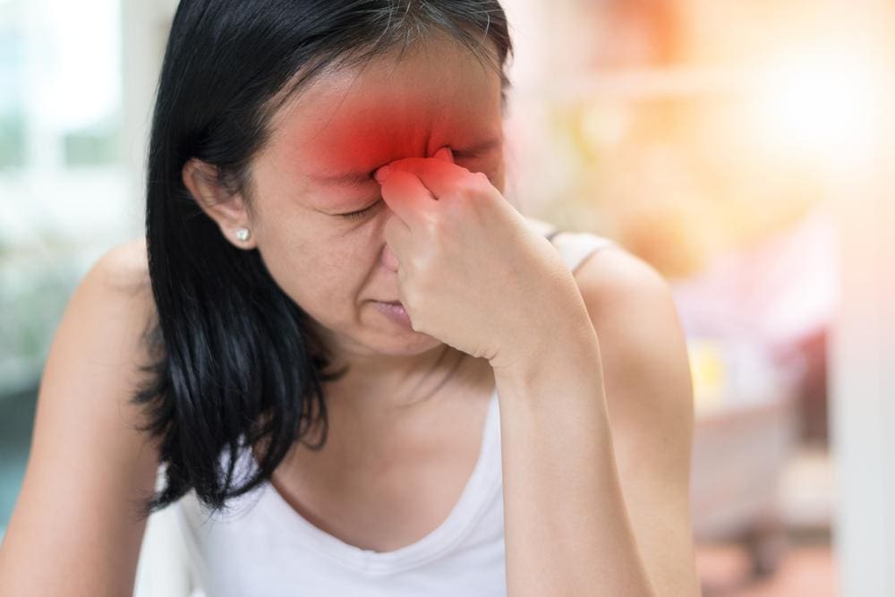 A woman is wincing and holding her nose because she is suffering from sinus headaches.
