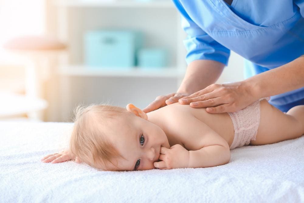 A chiropractor is gently massaging a baby.