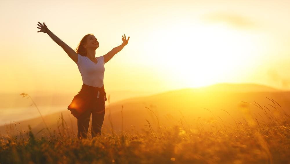 A happy woman is hiking in a hill at sunrise. 