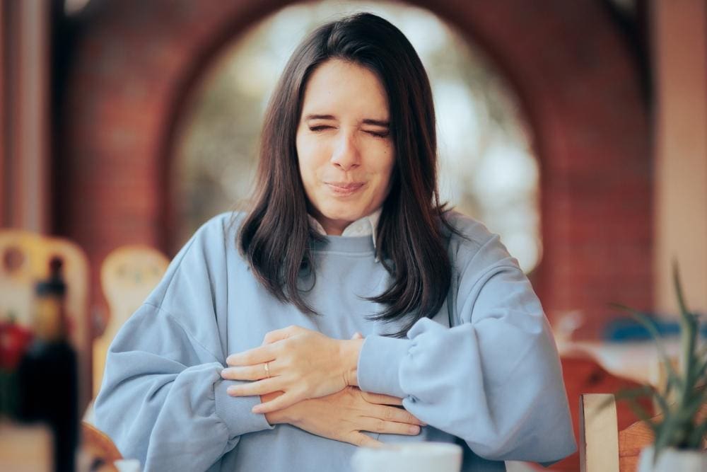 A woman is wincing and holding her abdomen because of Hiatal Hernia pain.