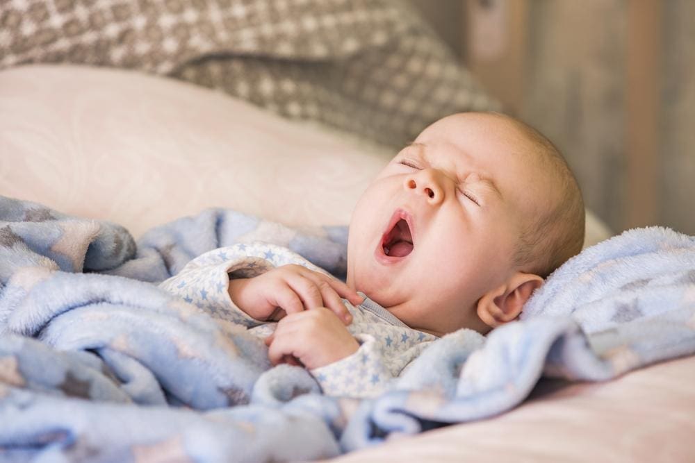 A baby is yawning and very sleepy.
One of the biggest reasons people struggle with sleep is their bodies don’t know the difference between night and day. Make sure your baby recognizes that nighttime is the time to relax and begin to feel sleepy. Dim the lights, quiet the environment, and make sure your baby isn’t overstimulated when it’s time for sleeping.
Pacifier
Although there are varying opinions regarding pacifier use, they can be a good tool for soothing your baby and preparing them for sleep. Some parents opt only to use pacifiers for naps and bedtime.
Swaddling 
Swaddling has long been used to calm babies. Snuggly wrapping your baby gives the sensation that they are back in the womb. It’s proven to help with sleep, especially for babies with neurologic issues and colic.


It’s also believed to reduce the risk of sudden infant death syndrome (SIDS). Babies should sleep on their backs, but some struggle to fall and stay asleep in this position. Swaddling makes them feel secure and avoids their urge to startle themselves awake when on their backs.
Adapt to your baby’s preferences (within reason) 
Every baby is different. If you find something that works for your baby when it comes to sleeping, and it’s within reason, there’s no reason why you shouldn’t do it. 


A good example is your baby’s sleep schedule. You might prefer your baby to wake and sleep at a particular time, but sometimes babies just won’t adjust to the parent’s preferences. If your baby likes to awaken at dawn and go to sleep before sunset, even if it’s not your preference, it might be best to adjust.

