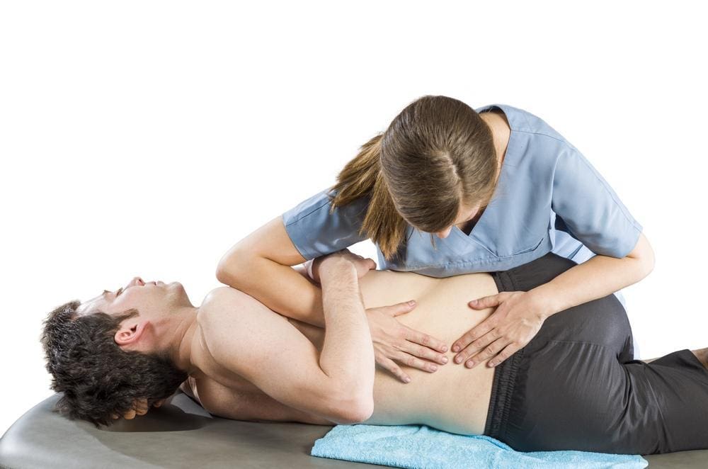 Chiropractor manually manipulating hip of young male patient.
