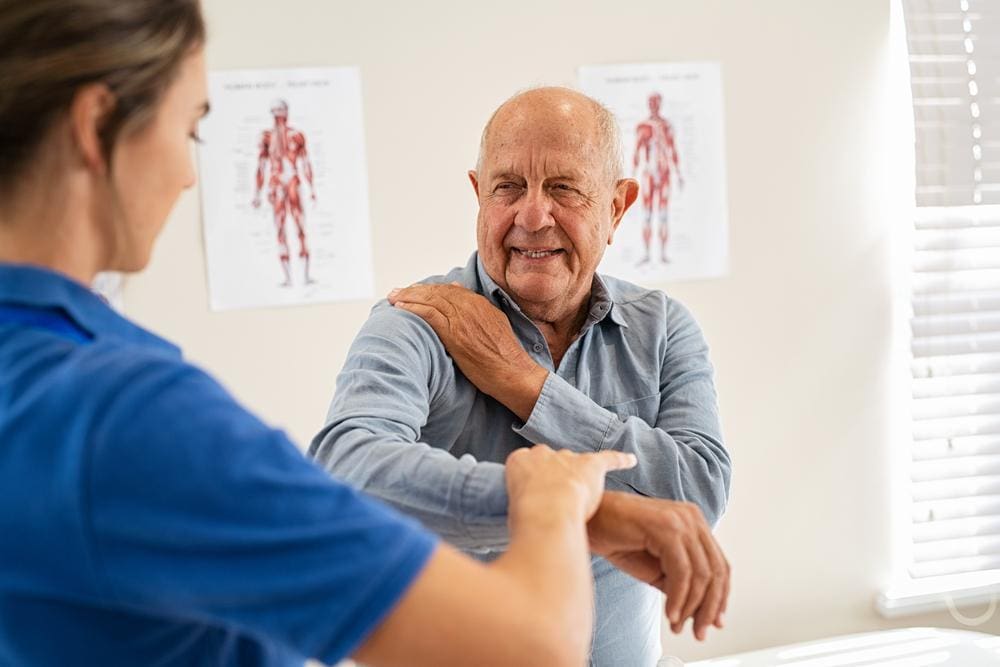 Chiropractor helping senior man with arm stretches.
