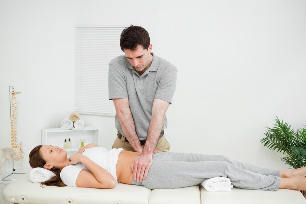 Chiropractor adjusting abdomen of woman lying on her back on treatment table.