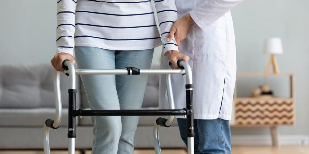 A doctor is helping a woman walk with a walker.