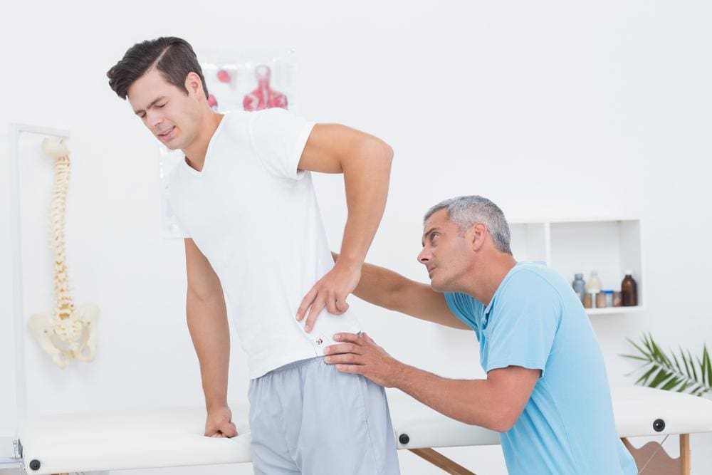 Chiropractor examining back and hip of young male patient.
