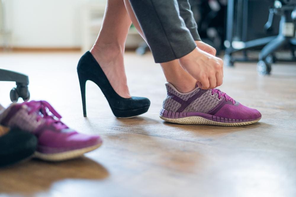 A woman is changing out of high heels into comfortable sneakers. 