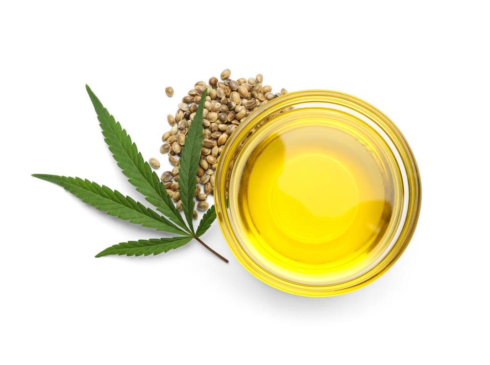 A small bowl of CBD oil next to seeds and a marijuana leaf.