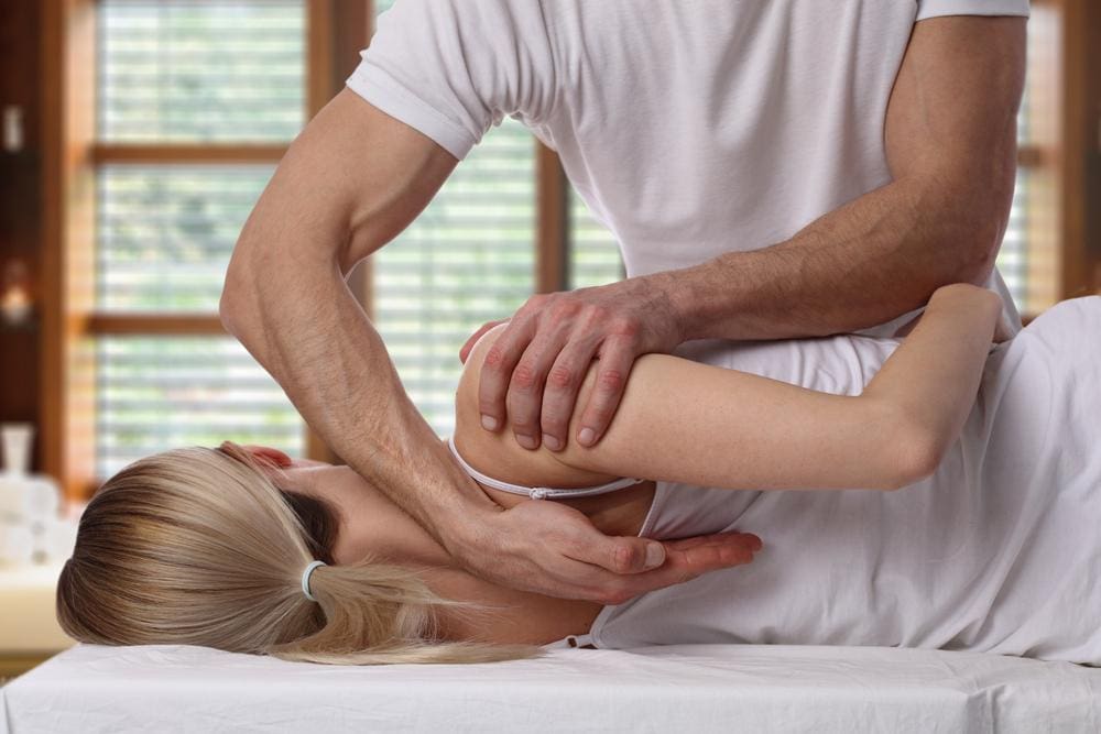 Young blond woman having her neck and back adjusted by chiropractor.
