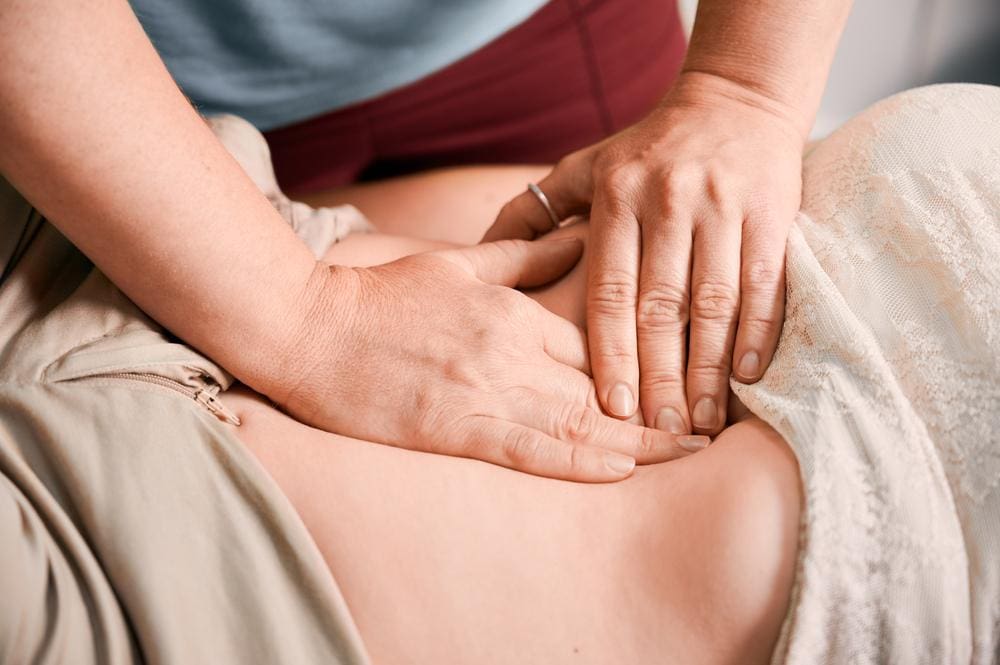 A chiropractor is massaging woman's abdomen to manage GERD. 
