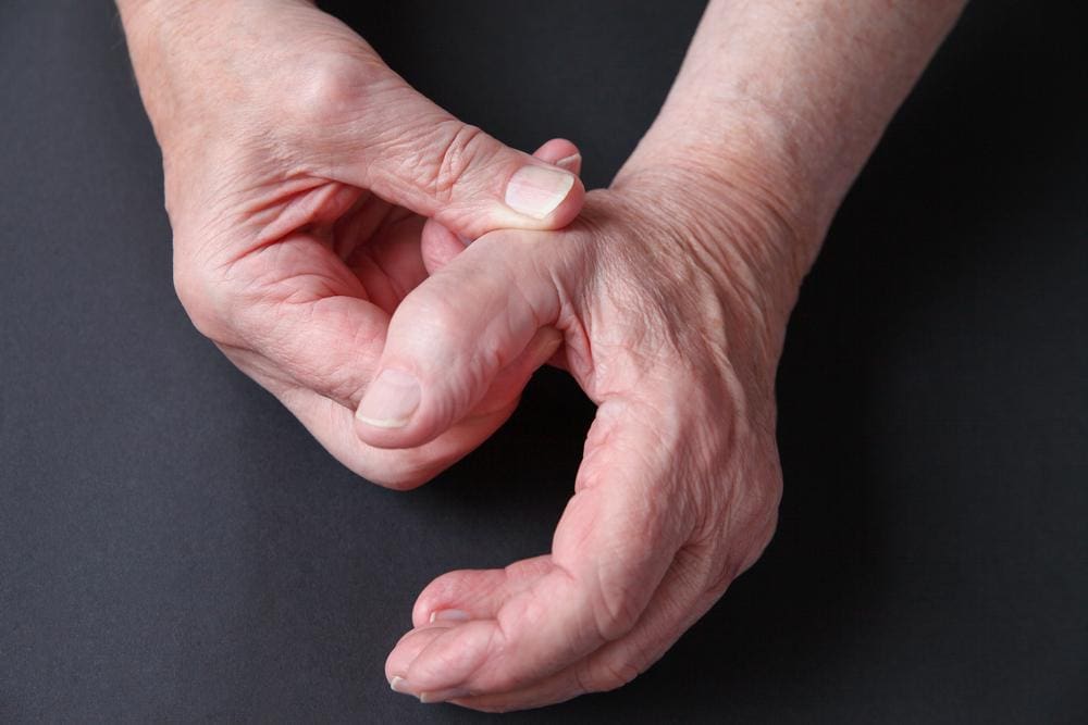 Elderly man massaging his thumb affected by CMC arthritis.
