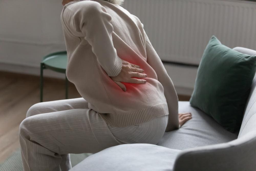 A woman is struggling to get up from the couch because of lumbar pain. 
