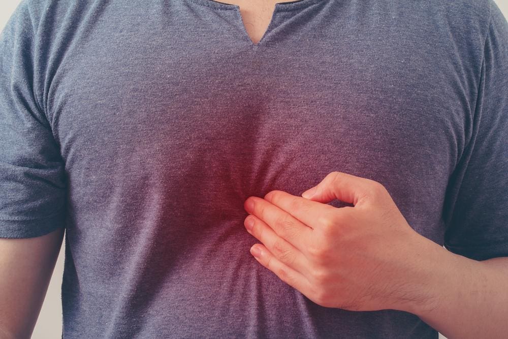 A man suffering from GERD is pressing his fingers to his chest.