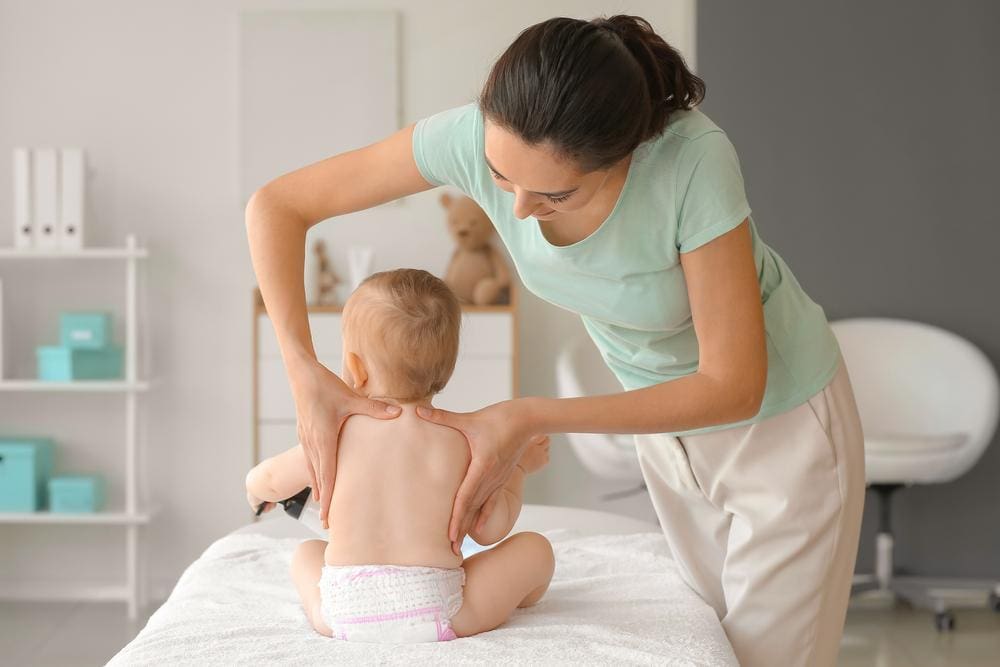 Chiropractor massaging back of infant sitting on treatment table.
