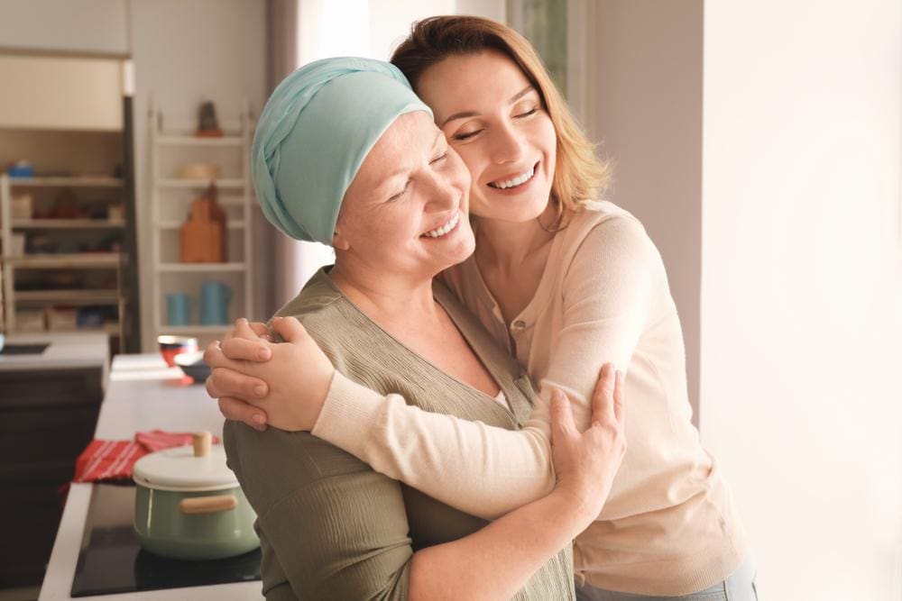 Young woman embracing her mother who is undergoing cancer treatment.
