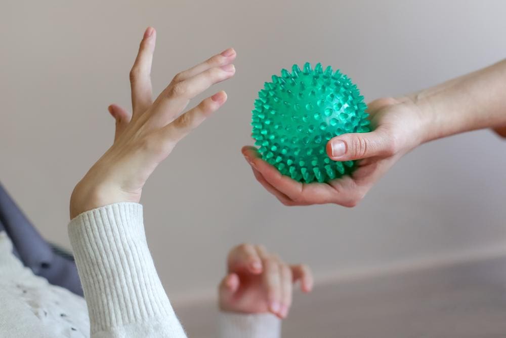 Girl with cerebral palsy reaching for green exercise ball.