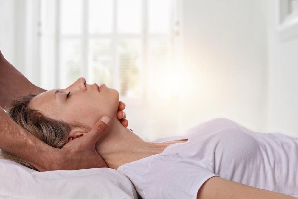 Woman lying on her back having her neck adjusted by a chiropractor.