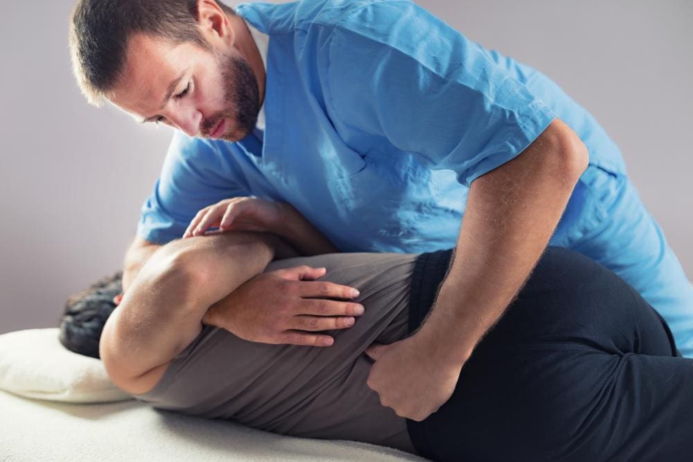 Chiropractor stretching and adjusting back of male patient.
