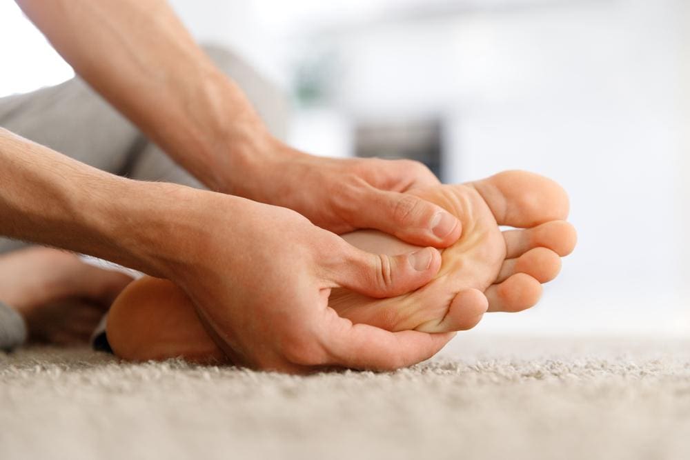 Man sitting on the carpet giving himself a foot massage.