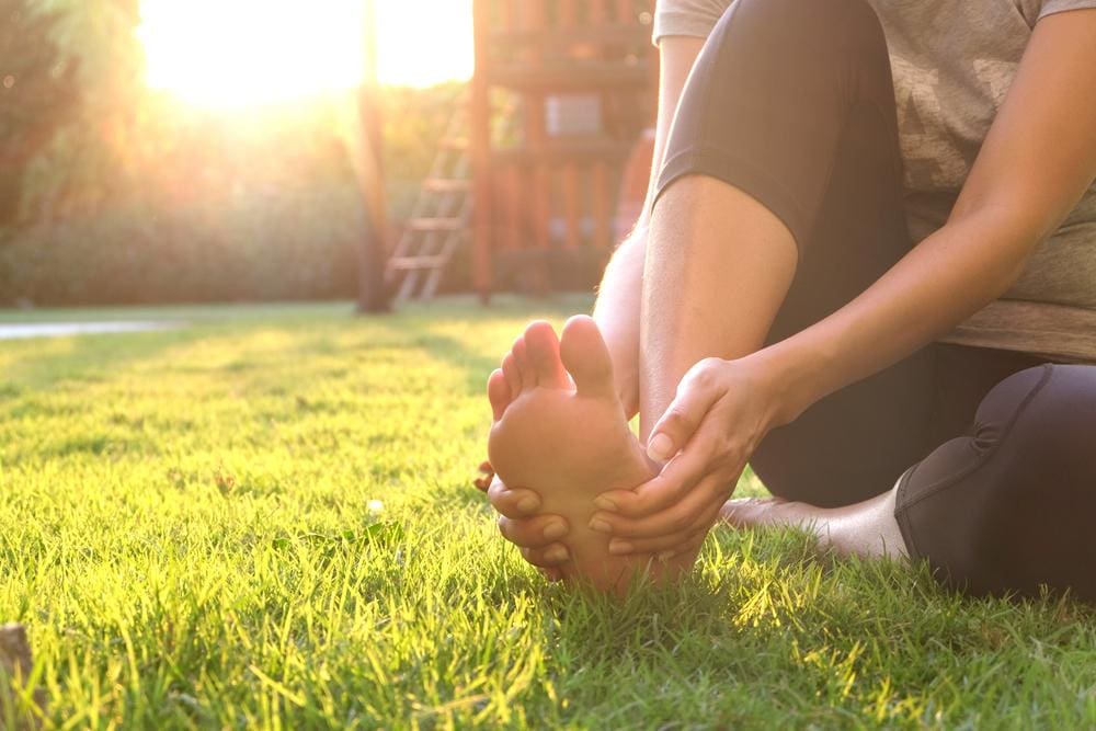 Woman sitting on the grass grasping the bottom of her foot.
