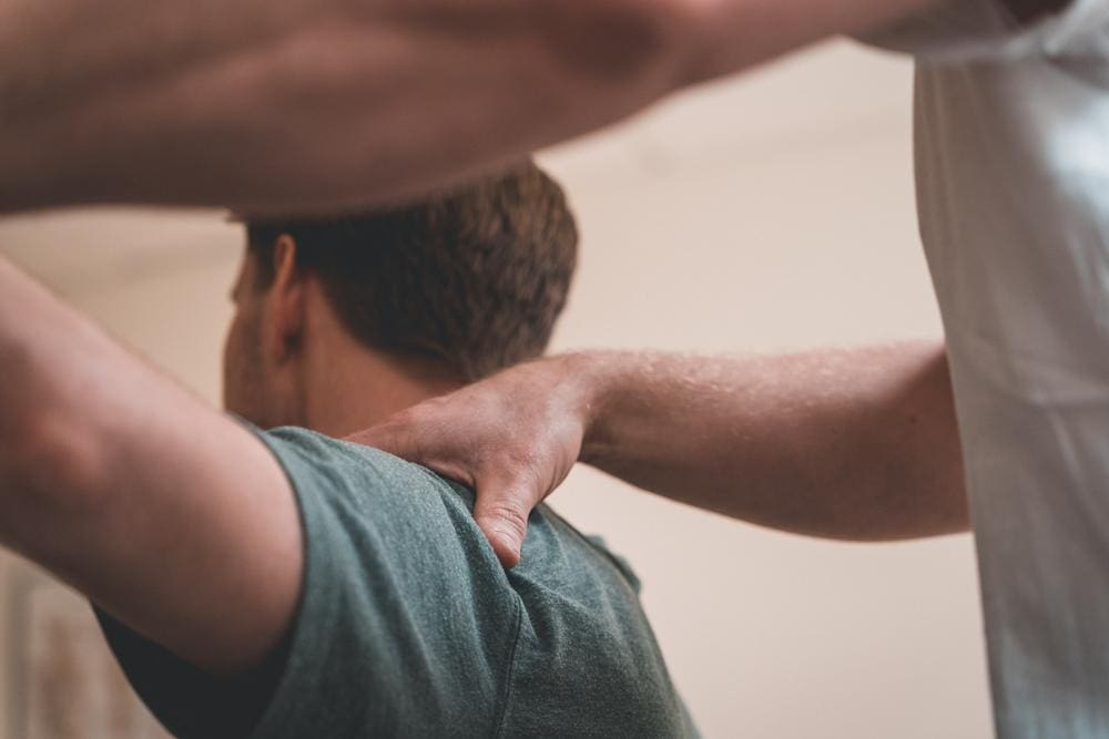 Chiropractor adjusting shoulder of male patient with radiculopathy.