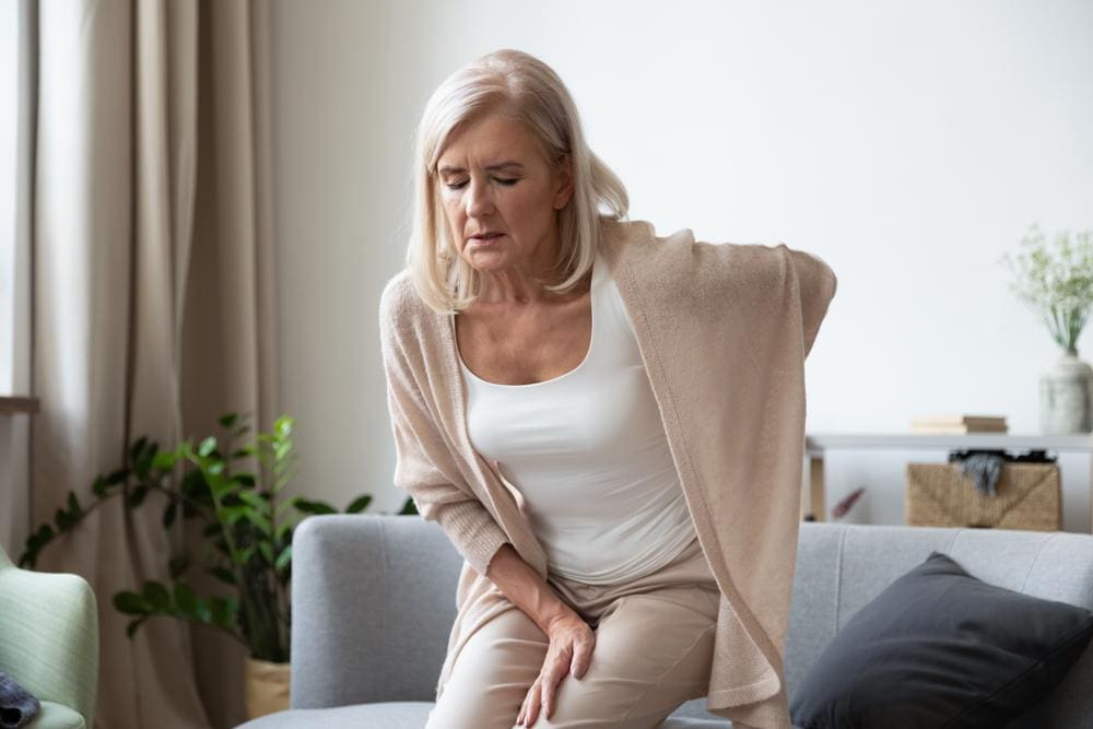 Older woman suffering from radiculopathy getting off a couch.