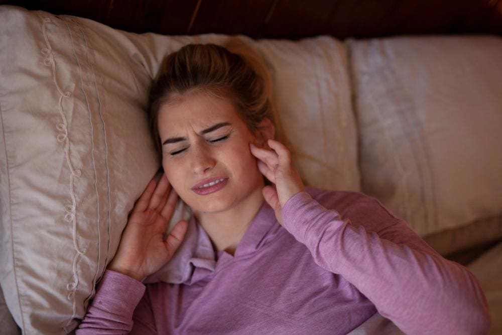 Young woman lying in bed holding both sides of her jaw.