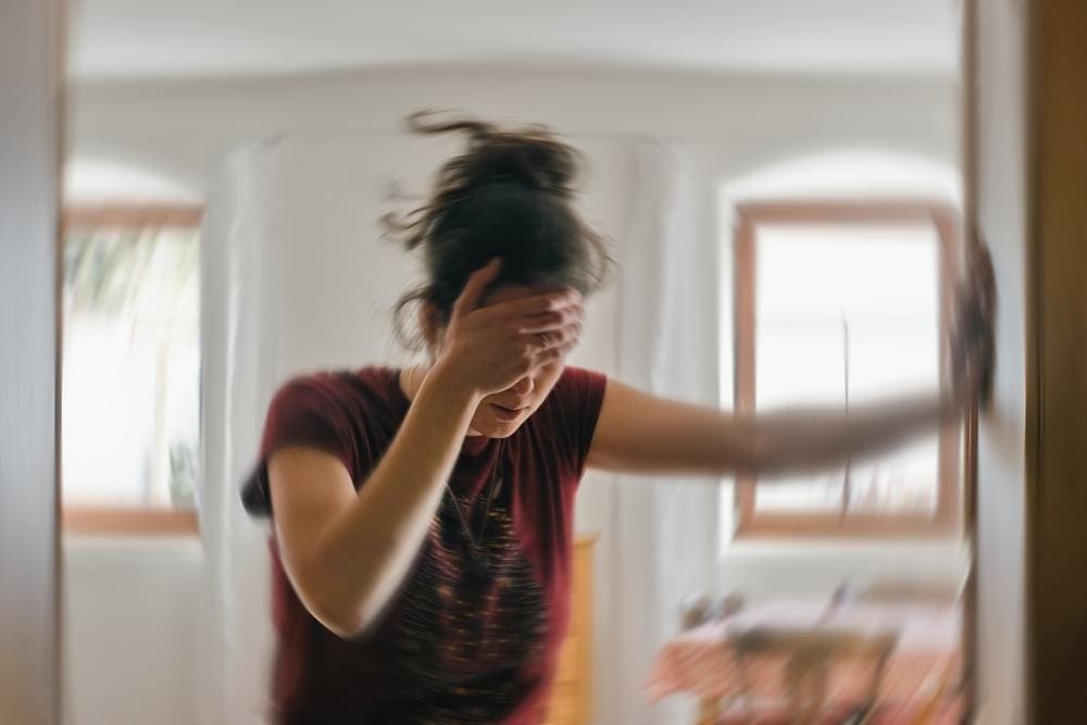 Blurred image of woman suffering from vertigo leaning against wall.