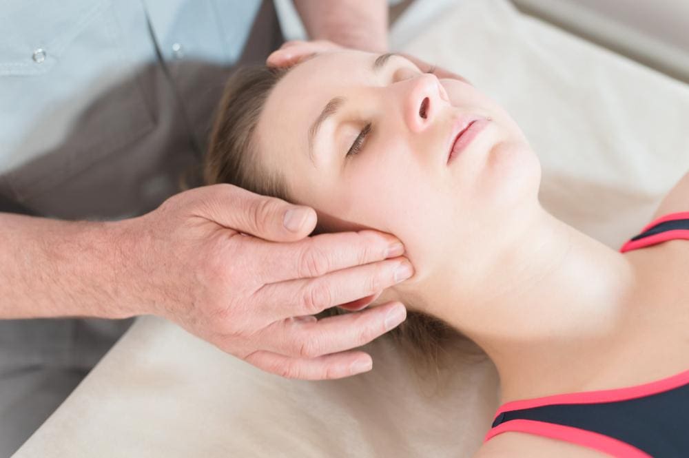 Chiropractor adjusting jaw of woman suffering from TMJ disorder.