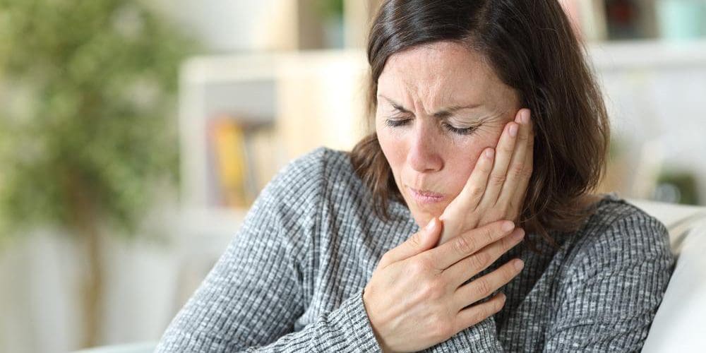 Middle-aged woman suffering from TMJ pain holding the side of her face.