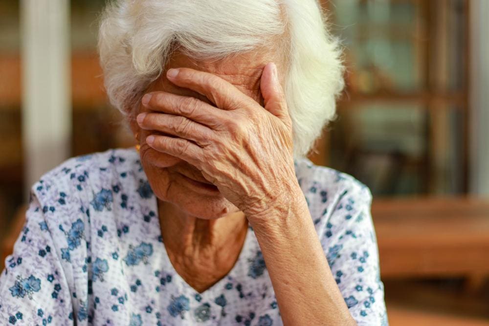An older woman with covers her face with her hand, distraught. 