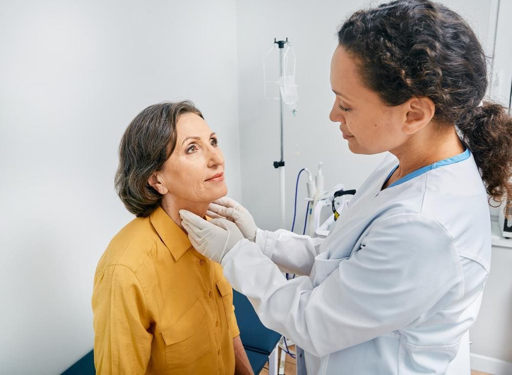 Doctor feels an older woman's thyroid gland.