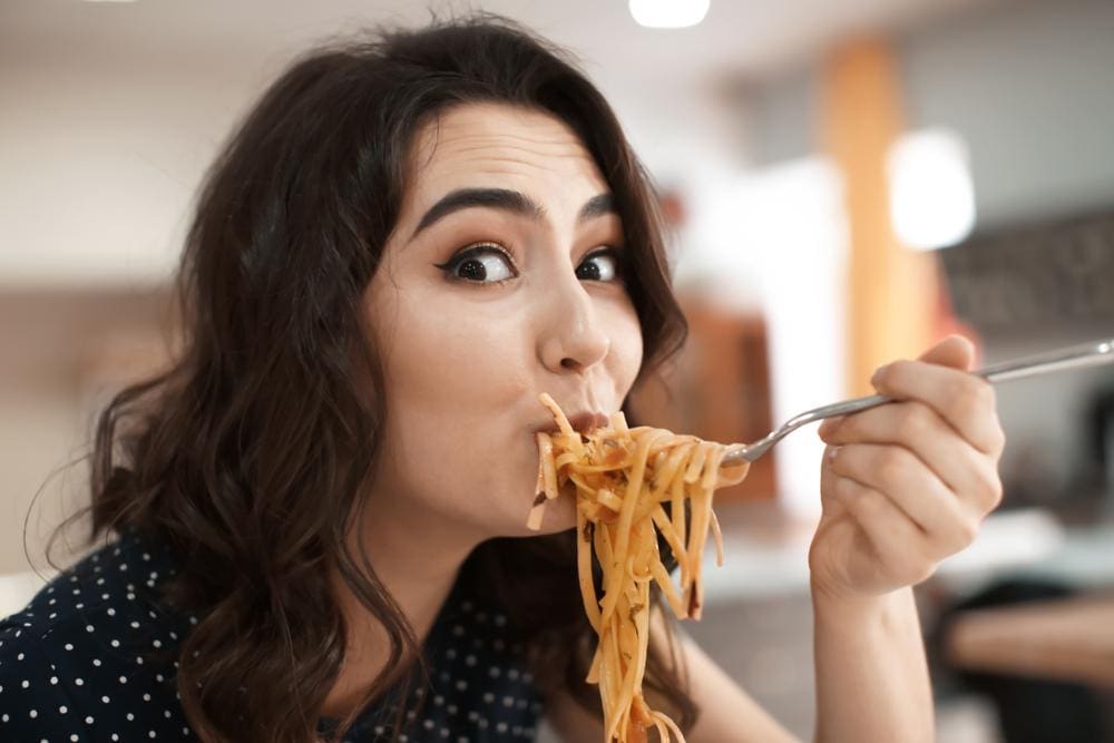 Happy young woman eating pasta.