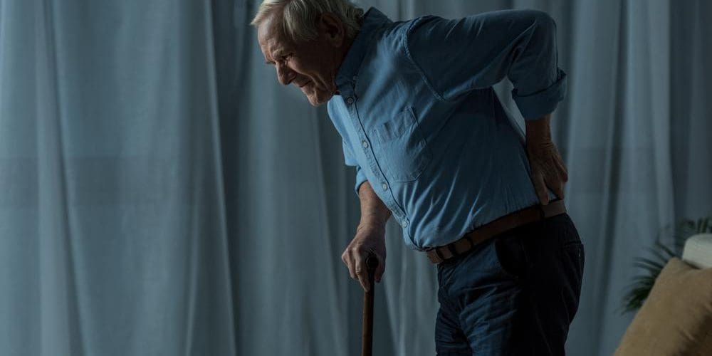 Senior man with back pain using a cane.